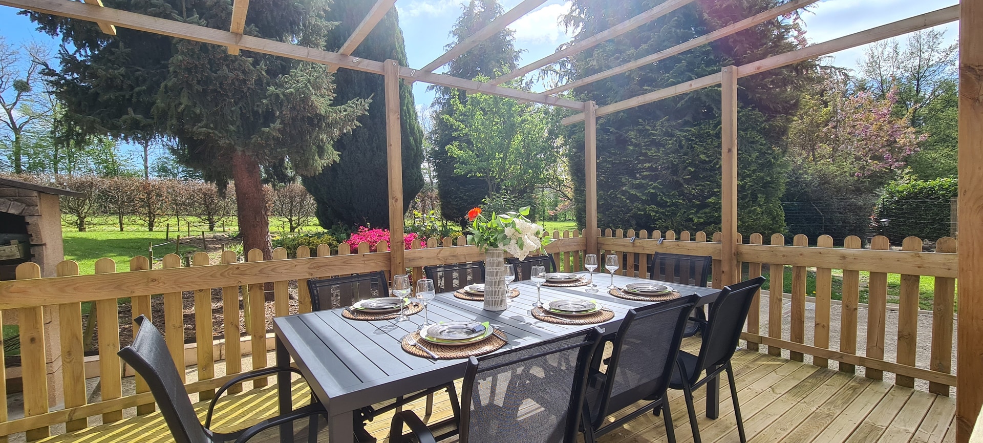 Terrasse en bois avec table dressée face au jardin arboré.